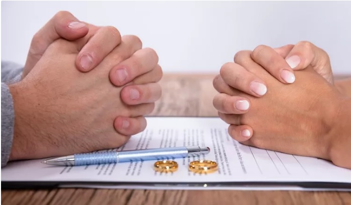 mãos fechadas, alianças, caneta e documento do divórcio